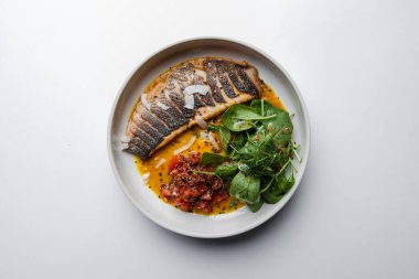 Soslu ızgara balık ve tabakta otlar.