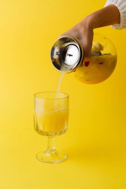 Sarı arka planda bir bardağa tropikal meyve suyu döken kadın eli manzarası