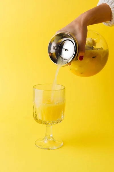 女性的手将热带果汁倒入黄色背景的杯子中 — 图库照片