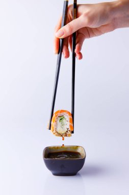 Kadın eli Japon suşisini yemek çubuklarıyla tutuyor ve teriyaki sosunu beyaz arka plana batırıyor.