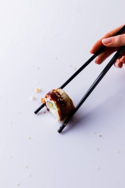 Kadın eli yemek çubuklarıyla Japon suşisi, beyaz arkaplanda teriyaki soslu Japon uramaki.