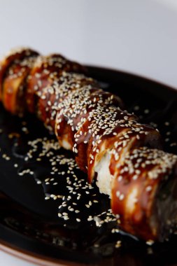 Beyaz zemin üzerinde teriyaki soslu Japon uramaki.