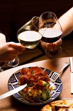Bardakları tokuşturup restorandaki masada yemek yiyen insanların görüntüsü.