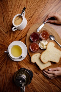 Kadın tostun üstüne meyve reçeli sürüyor.