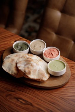 Ev yapımı humus ve ahşap masadaki soslarla pitaların yakın görüntüsü.