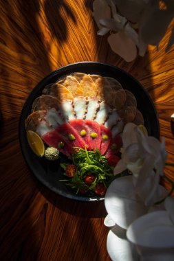 Lezzetli deniz ürünleri ve limon dilimlenmiş tabak, otlar, ahtapot dokunaçları, somon parçaları ve eski ahşap bir masada kırmızı balık filetosu.