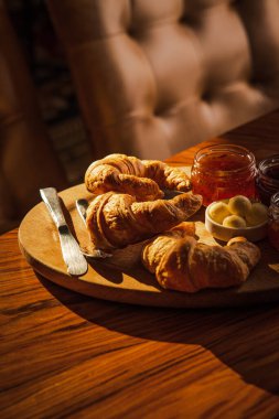 Tahta üzerinde lezzetli çıtır kruvasanlar reçel kavanozları ve şeker kamışı ile ılık ışıkta