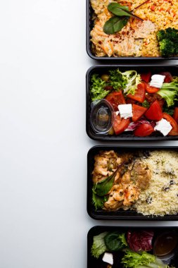 Beyaz arka planda çeşitli yiyecek ve sebze salatası olan beslenme çantalarının üst görüntüsü