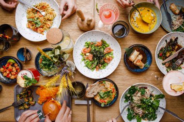 Servis masasının üst görüntüsü, çeşitli yemekler ve masada yemek yiyen insanlar.