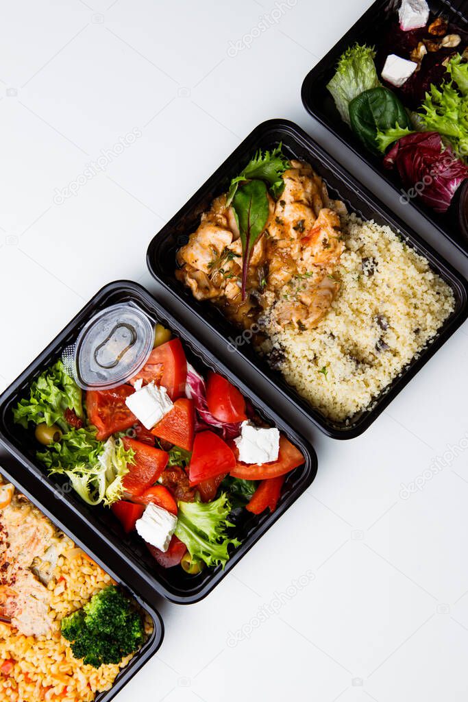 top view of lunchboxes with various food and vegetable salad on white background