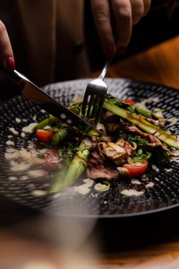 Siyah tabakta kuşkonmaz ve sebzeli sulu bifteğin yakın plan görüntüsü.