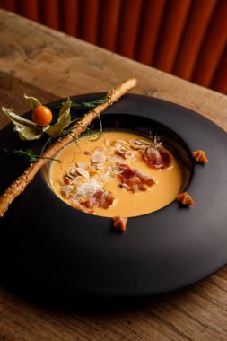 Yakın plan balkabağı çorbası pastırma ve siyah tabakta susamlı pipet.