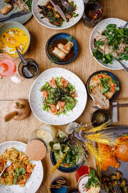 Servis masasının üst görüntüsü, çeşitli yemekler ve masada yemek yiyen insanlar.