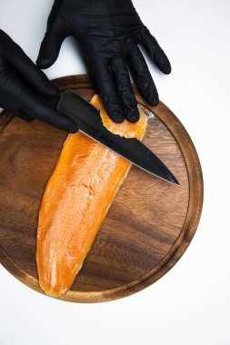 Şefin elleri beyaz arka planda izole edilmiş kırmızı balık filetosunu keserken görülüyor 
