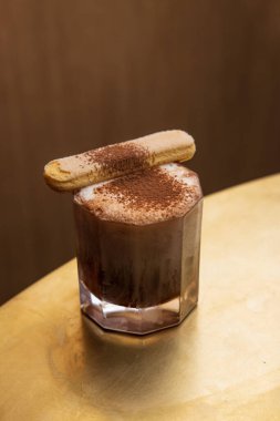 Çikolata tozu ve Savoiardi kurabiyesiyle süslenmiş tiramisu tadı olan bir kokteyl.