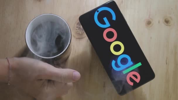 Android智能手机上的谷歌标志 上面有木制桌子上的热咖啡 — 图库视频影像