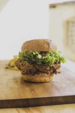 Kızarmış tavuk ve salatalı hamburger. Marullu sandviç, domates, soğan, avokado, salatalık ve tavuk. Ahşap kesim tahtasında yeşil salatalı ticari kullanım hamburgeri. Kızarmış tavuk.. 