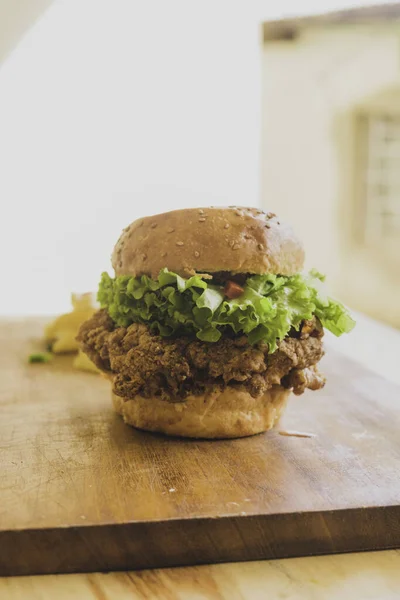 Hamburgers with fried chicken and salad. Sandwich with lettuce, tomato, onion, avocado, cucumber and chicken. Commercial use burger with green salad on a wooden cutting board. Batter-fried chicken.