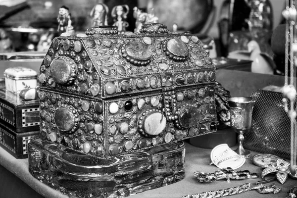 Iron chest full of stones and jewels on a table. There are golden pieces together and other objects. (Black and white version)