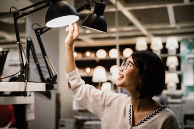 Asyalı genç, kısa saçlı, gözlüklü güzel kadın mobilya mağazasından yeni lamba almayı seçiyor.