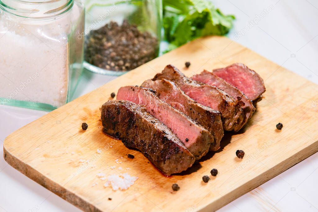 Grilled beef filet Mignon steak or tenderloin on wooden board with pepper, salt and coriander leaves