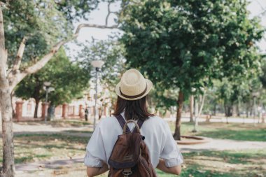 Behind of young asian woman with backpack and straw hat walking in park