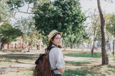 Young asian woman with backpack and straw hat walking in park