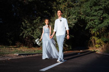 Ormanda ve göl kenarında akşam yürüyüşüne çıkmış mutlu genç bir çift. Gelin mavi bir gelinlik giyiyor..