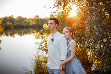 Ormanda ve göl kenarında akşam yürüyüşüne çıkmış mutlu genç bir çift. Gelin mavi bir gelinlik giyiyor..