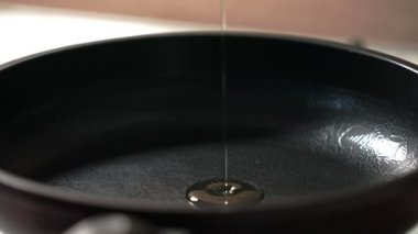 Sıcak, siyah bir tavaya zeytinyağı dökme süreci. Yavaş çekimde, ayçiçeği yağı siyah bir tavaya dökülür. yavaş çekim