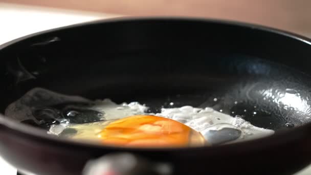 Il processo di produzione di uova strapazzate da un uovo in una padella nera. Al rallentatore. macro ripresa — Video Stock