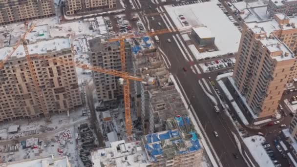 O processo de construção de casas modernas no inverno. Vários guindastes de torre amarela constroem casas modernas no inverno em um dia nevado. construtores no topo. vista aérea — Vídeo de Stock