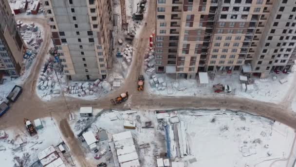 Yellow tractor excavator drives on the construction site of modern houses on a winter day, aerial view — Stock Video