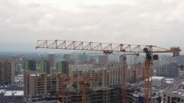 Sarı kule vinci, diğer vinçlerin arka planına karşı büyük bir inşaat alanının yüksekliğinde çalışıyor. Yukarıdan görünüm