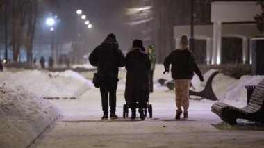 Kışın kar yağarken bebek arabasında bir aile gece parkında yürüyor. arka plan
