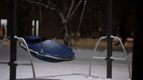 Balançoire se balançant sur une aire de jeux complètement vide lors d'un confinement dans une forte chute de neige. pendant la pandémie de covidé-19. Mouvement lent — Video