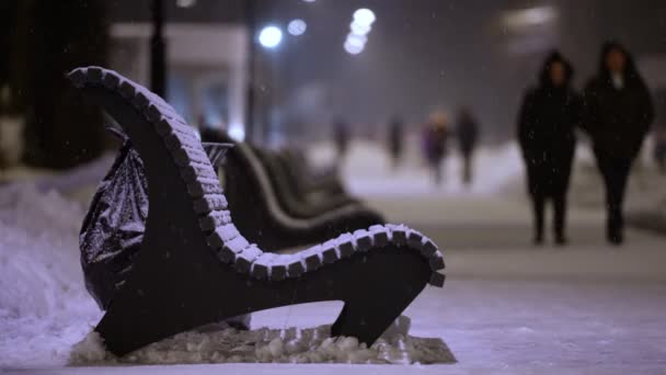 Bancos de rua vazios no parque durante a queda de neve pesada à noite. as pessoas querem ao redor — Vídeo de Stock