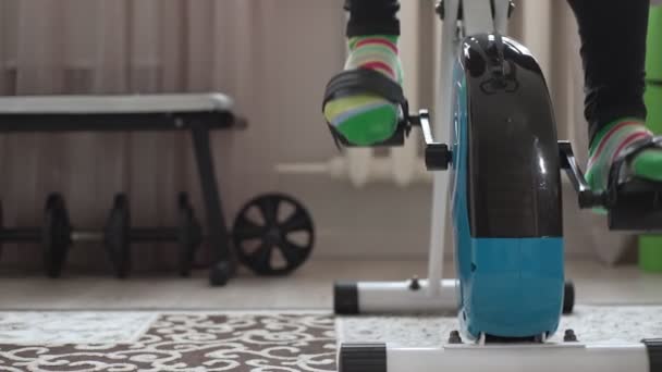 Ноги, що педалюють вправи на велосипеді вдома в кімнаті, вид крупним планом. ляльковий знімок камери — стокове відео