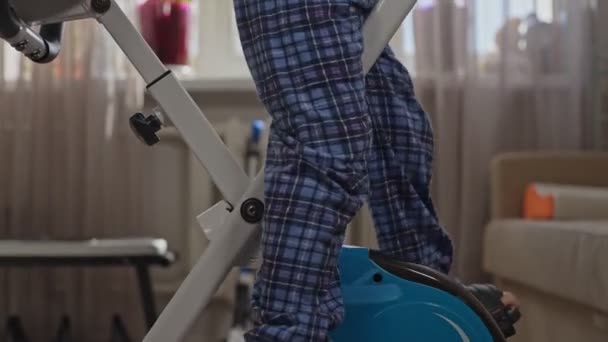 Mały chłopiec w domu ubrania pedałuje rower treningowy w domu w pokoju — Wideo stockowe