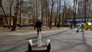 Küçük çocuk, baharın başında yeni teknoloji segway aletinin yardımıyla oyun sahasında oyun oynuyor.