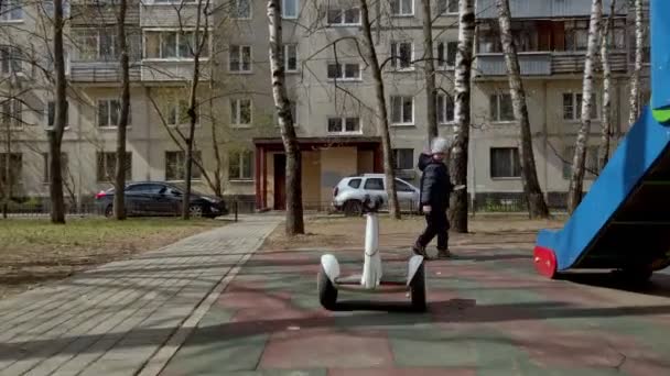 Pequeño niño divertido jugando en el patio de recreo con la ayuda de la nueva tecnología gadget segway a principios de primavera — Vídeos de Stock