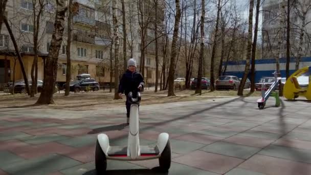 Pequeño niño divertido jugando en el patio de recreo con la ayuda de la nueva tecnología gadget segway a principios de primavera — Vídeos de Stock