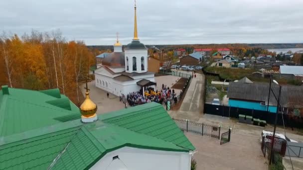 Крестный ход вокруг храма священниками во время православного праздника, в живописном месте на фоне пейзажа золотой осенью — стоковое видео