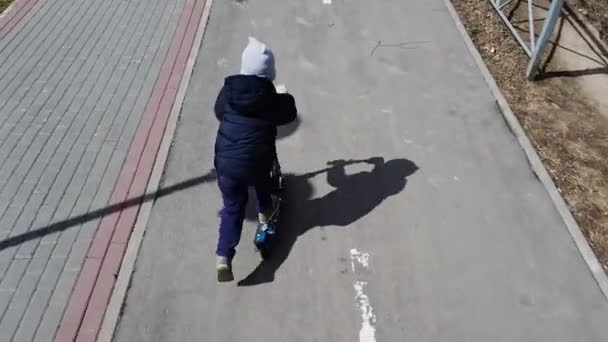 Little boy riding a scooter on a city bike path in early spring — Stock Video