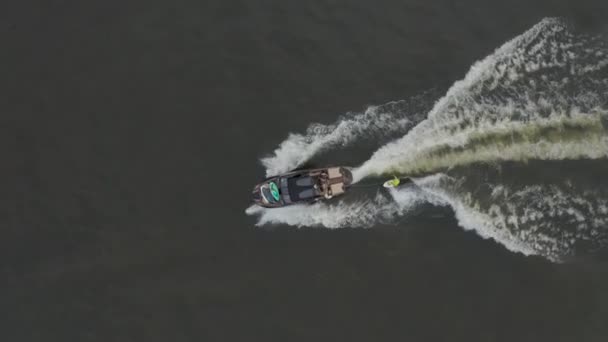 Vista aérea de la mujer montando wakeboard detrás de la lancha en el lago, deportes acuáticos, tiro de seguimiento. Entrenamiento de wakeboard en el río. Un barco con una chica atleta se mueve sobre el agua. — Vídeo de stock