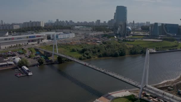 Μια τεράστια σύγχρονη λευκή πεζογέφυρα κατά μήκος του ποταμού με φόντο την κυβέρνηση της περιοχής της Μόσχας. Αεροφωτογραφία — Αρχείο Βίντεο