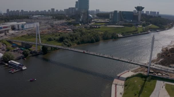 Een enorme moderne witte voetgangersbrug over de rivier tegen de achtergrond van de regering van de regio Moskou. luchtzicht — Stockvideo