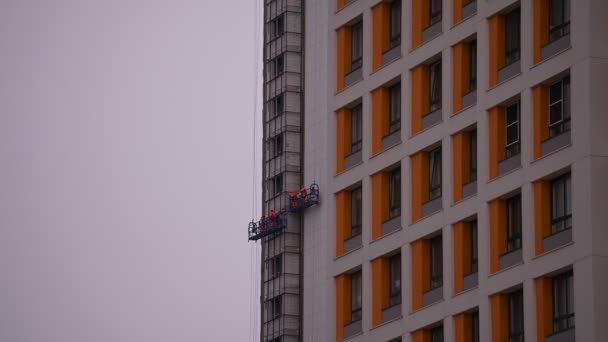 高層ビルが高層ビルの中に建てられ、近代的な家が建てられています。高さの建設クレードルの高高度登山者は. — ストック動画