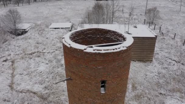 Cihlová opuštěná vodní věž uprostřed lesa a opuštěné budovy v zimní krajině. zobrazení vzduchu — Stock video