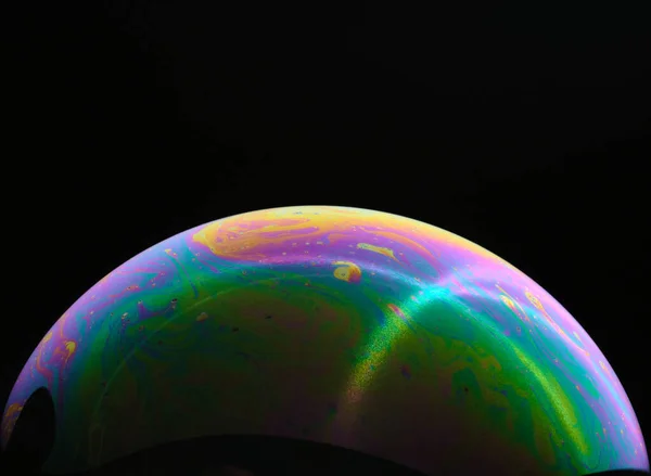 A bubble in rainbow colors on a black background. Close-up. Side view. Bright colors. Imitation of an unknown planet.